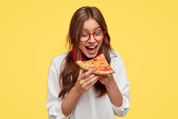 Hungry student opens mouth widely while sees delicious slice of pizza, wants to eat, dressed in...