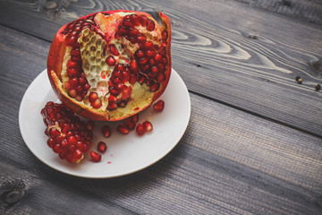 Pomegranate burst ripeness on a white plate on a light wooden table top.