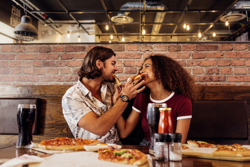 Smiling couple feeding each other pizza