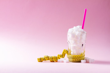 Sugar in glass with measuring tape on on pink background with copy space
