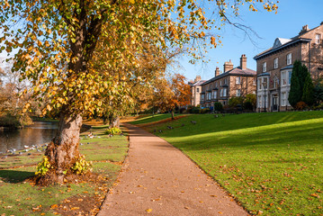 Walkway through a beautiful autumn park with stone Georgian houses and autumnal trees, taken in Buxton Park UK in fall on a sunny day.