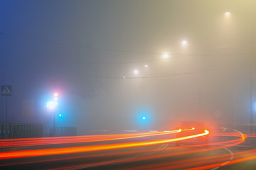 city street at night in heavy fog, traces of headlights of cars on a long exposure