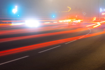 city street at night in heavy fog, traces of headlights of cars on a long exposure