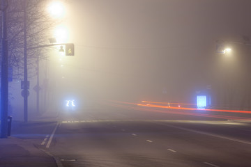 city street at night in heavy fog, traces of headlights of cars on a long exposure