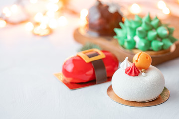 Mini mousse pastry desserts covered with velour or glaze. Garland lamps bokeh on background. Modern european cake. French cuisine. Christmas theme.