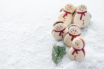 Variety of sweet macaroons. Cookie in the form of a snowman on gray table sprinkled with snow. Modern european French cuisine. Christmas theme, Merry Christmas card. New year mood.