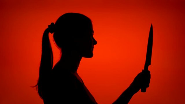 Silhouette of young scary woman holding sharp blade. Female's face in profile with dangerous knife on red background. Black contour shadow of teenager's half-face. Violence and aggression concept