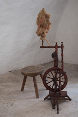 old spinning wheel and wooden stool in an almost empty white room 