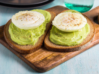 Fototapeta na wymiar Rye bread avocado toasts with poached egg on wooden serving board. Brunch lunch meal