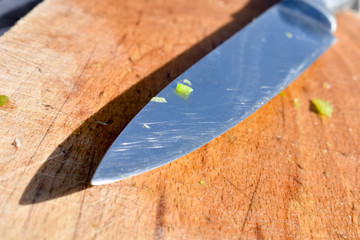 Diagonal view of one used metallic knife on top isolated proyecting its shadow on a wet wooden board. Rests of organic cuisine foods.