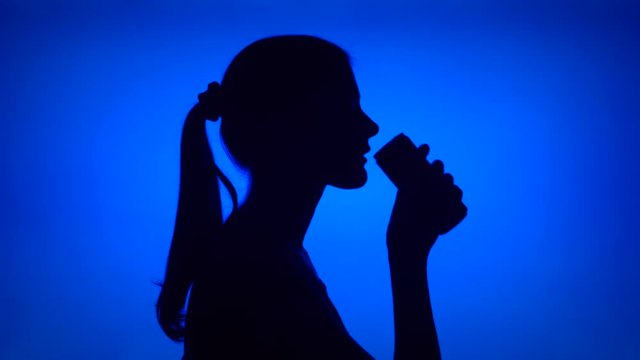 Silhouette of young woman opening can of soft drink on blue background. Female's face in profile drinking soda from tin. Black contur shadow of teenager's half-face