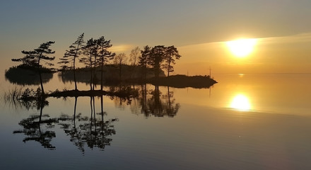 Fototapeta na wymiar Fantastic sunset and reflections of islands and trees in calm water.