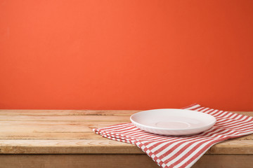 Empty white plate with tablecloth on wooden table over red wall  background