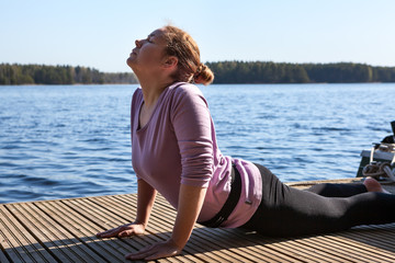 Fototapeta na wymiar Stretching exercise at the pier near the lake, yoga with breath control and simple meditation