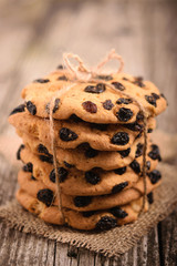 Homemade oatmeal cookies with raisins, tied with a rope, lying in piles on a dark wooden background, morning sun