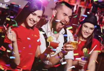 A group of friends at a party in a nightclub clink glasses with alcoholic beverages.