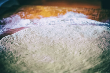 Making homemade pizza in a country kitchen with an overhead view of rolled out dough for the base with a wooden rolling pin on oven paper on an old wooden chopping board