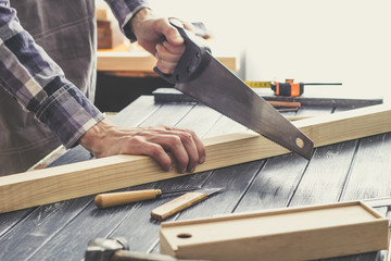 Carpenter sawing off a wooden plank in the workshop.  - obrazy, fototapety, plakaty