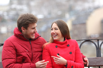 Happy couple talking in a bench in winter