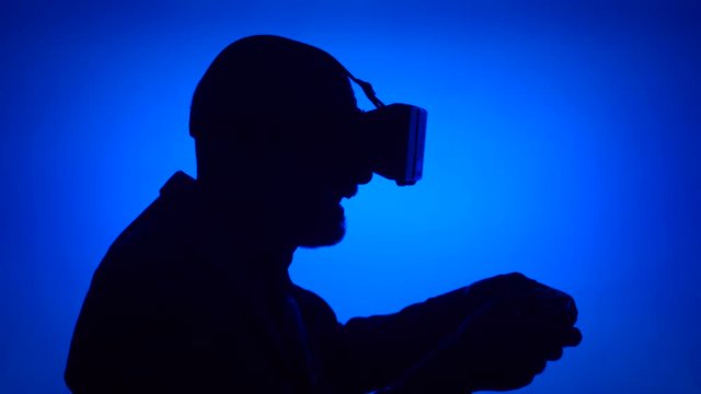 Black silhouette of senior man in VR 360 glasses play video game online. Male's face in profile with game console on blue background. Contour shadow of grandfather's half-face