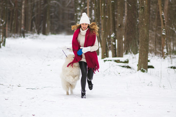Fototapeta na wymiar Pretty Young Woman in Snowy Winter Forest Park Walking Playing with her Dog White Samoyed Seasonal