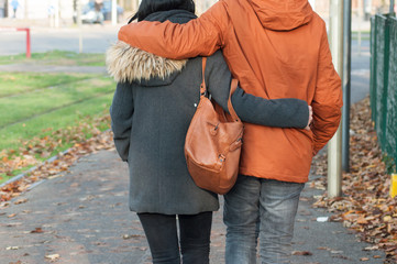 closeup of couple back entwined walking in the street by autumn