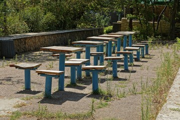 a row of old makeshift chairs and tables made of iron and boards on asphalt in the grass