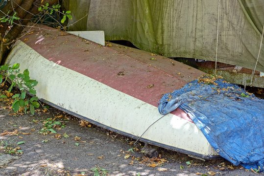 one old dirty inverted boat lies on the sidewalk in the street near the wall
