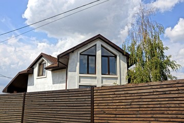 part of a white house with a window behind a brown wooden fence against the sky and clouds