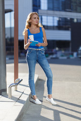 Beautiful young girl holding notebook and cup of coffe standing on the street. concept of business or education lifestyle