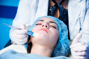 Model lying on couch with closed eyes. Doctor touching patient's face brush. Cosmetological clinic. Healthcare, clinic, cosmetology.