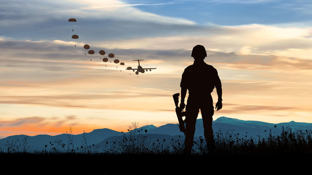 Silhouette of soldier at sunset watching the launch of paratroopers