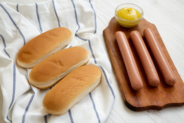 Ingredients for making hot dogs: sausages, hot-dog buns and mustard on white wooden background, side view. Close-up.