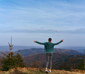 woman hiker with backpack, wearing in red jacket, standing on edge of cliff against a forest and foggy valley background