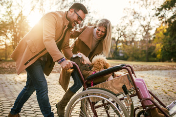Beautiful disabled girl in wheelchair enjoying with her mother, father and dog outdoors in park.