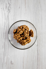 Walnuts in glass bowl over white wooden background, overhead view. Close-up. Flat lay, from above, top view.