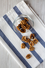 Walnuts in glass bowl over white wooden background, overhead view. Close-up. Overhead, from above.