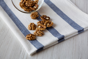 Walnuts in glass bowl over white wooden background, side view. Closeup.