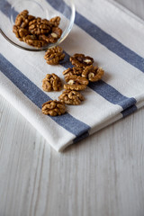 Walnuts in glass bowl over white wooden background, side view.