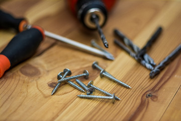 Drill, screwdriver and screws on a wooden table.