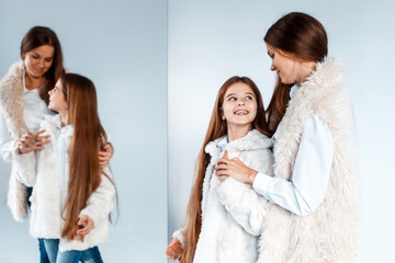 Stylish beautiful mother and a cute daughter with blue eyes in studio hugging and having fun