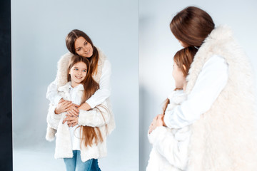 Stylish beautiful mother and a cute daughter with blue eyes in studio hugging and having fun
