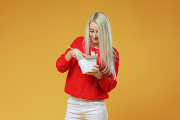 Bright blond woman eating asian fast food from takeaway box with chop sticks, Wok noodles concept