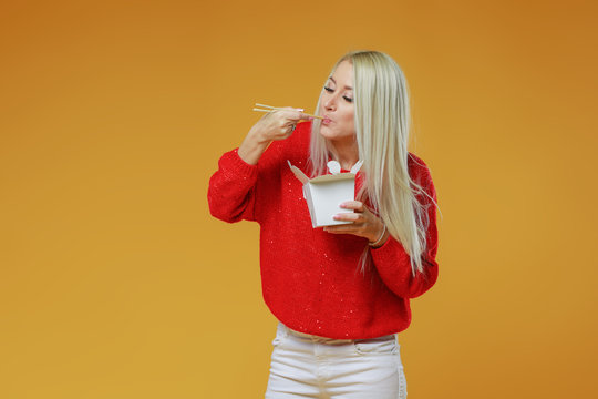 Bright blond woman eating asian fast food from takeaway box with chop sticks, Wok noodles concept