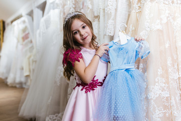 Fototapeta na wymiar Charming little girl choosing new elegant dress for her.
