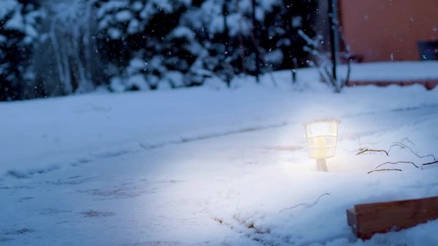 heavy snowfall with outdoor lights lit on a footpath during evening twilight