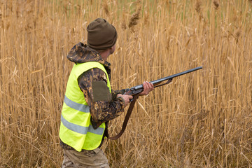 Hunter with a gun and a dog in the reeds in late autumn, Pheasant Hunting in a reflective vest