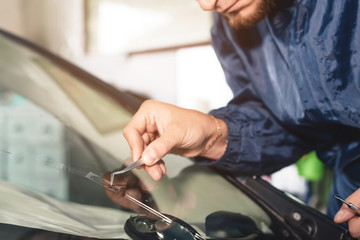 Close up Car glaze worker fixing and repairing a windshield or windshield of a car at a garage service station. Drill glass for repair