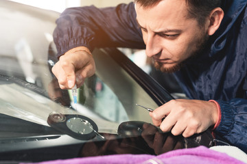 Close-up of a professional windshield repairman fills a crack in the glass with a special polymer...