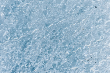 Obraz premium A close-up of the surface of a fragment of a glacier with a structure of strips and bubbles interspersed with sand and rocky rock. Ice blue texture to the light. Small DOF